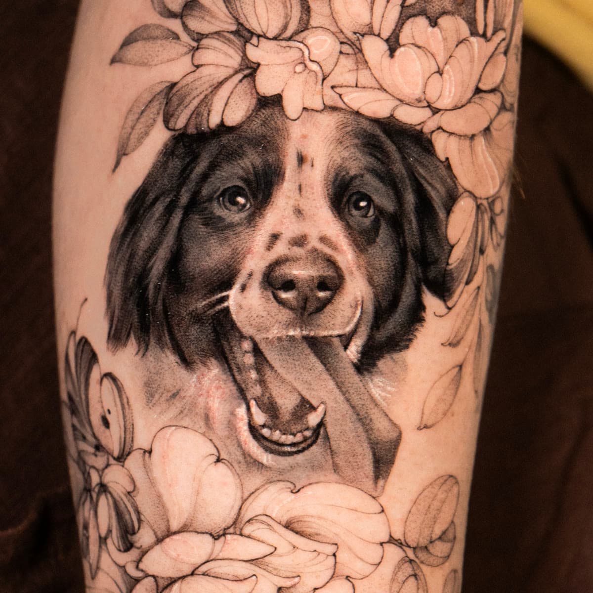 Black and grey tattoo of Tio's smiling face among peonies on a forearm